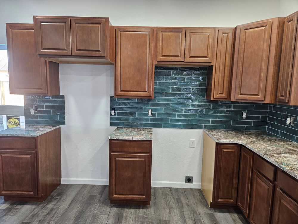 Kitchen with wood cabinets, blue tile backsplash, and gray countertops; cabinets are installed but appliances are missing.