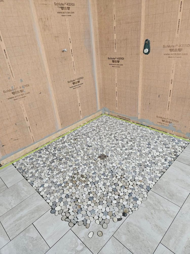 Shower stall with pebble floor, gray tiles, and orange waterproof wall panels.