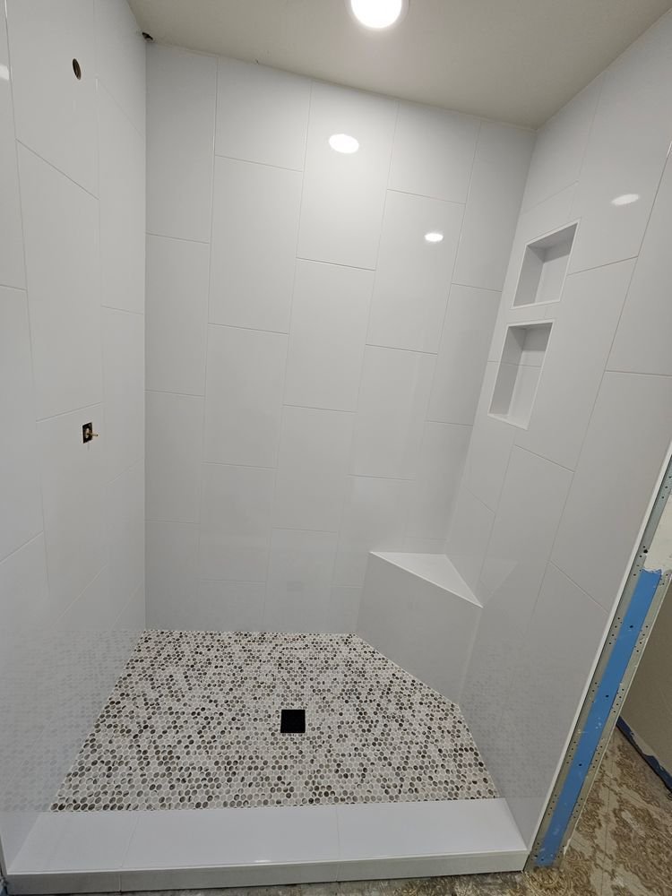 White tiled shower with mosaic floor, corner seat, and built-in shelf.