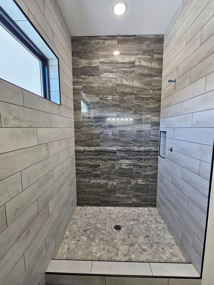 A modern shower with gray stone flooring and textured tile walls, a window, and a recessed shelf.