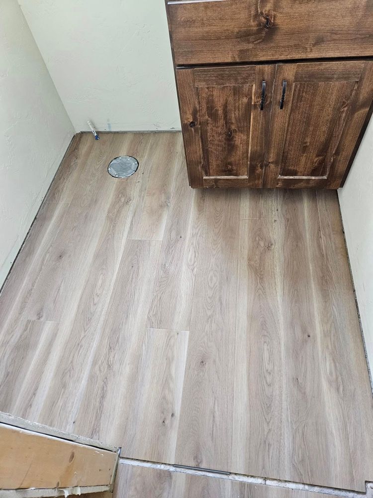 Light wood-look flooring installed in a small space with a brown cabinet overhead and a drain pipe.