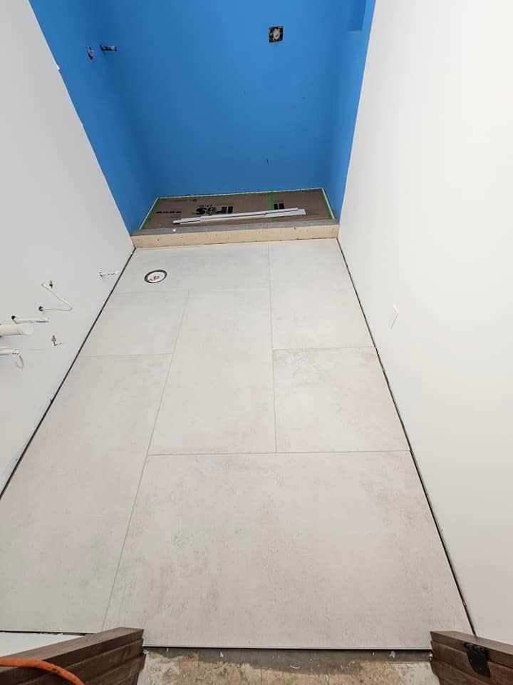 Narrow room with large white tiles on the walls and floor, blue ceiling.