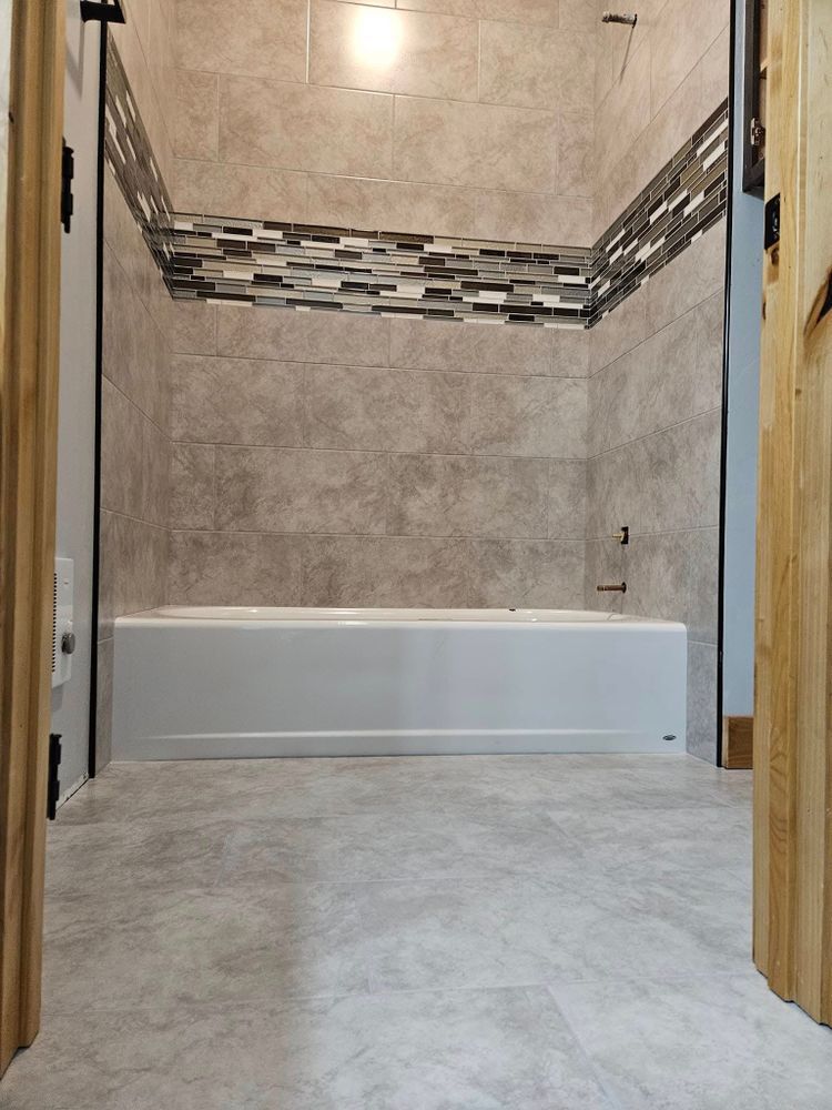Bathroom with a white tub, gray tile walls, and a decorative band of mosaic tile.
