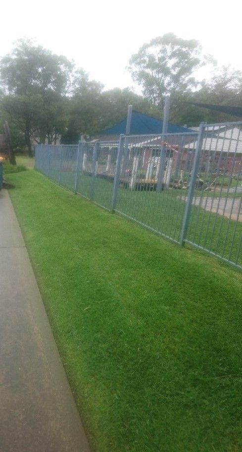 A person is walking down a sidewalk next to a fence.
