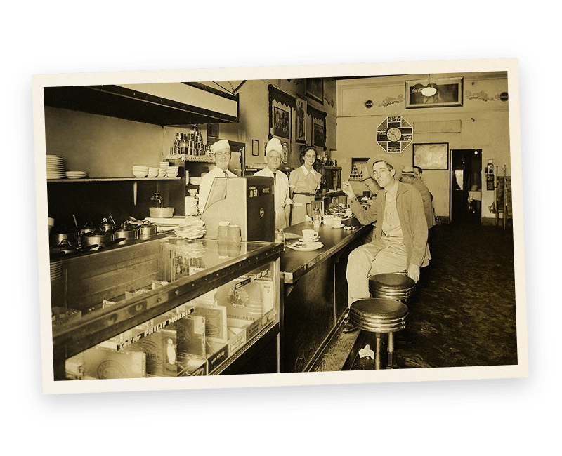 A black and white photo of people sitting at a counter in a restaurant.