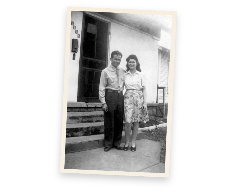 A black and white photo of a man and woman standing in front of a house.