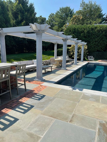 Backyard pool with white pergola, stone patio, and lounge chairs in bright sunlight