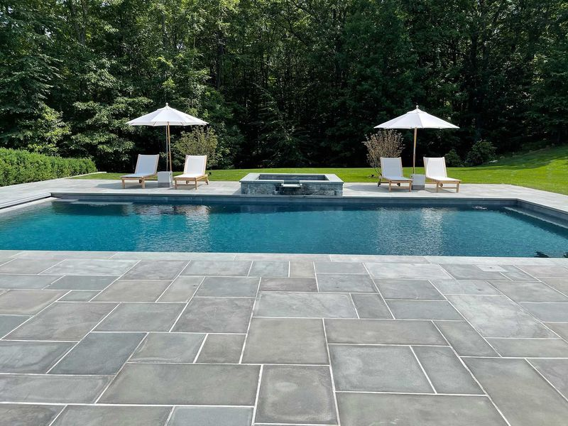 Backyard pool with stone patio, two white umbrellas, and lounge chairs surrounded by trees