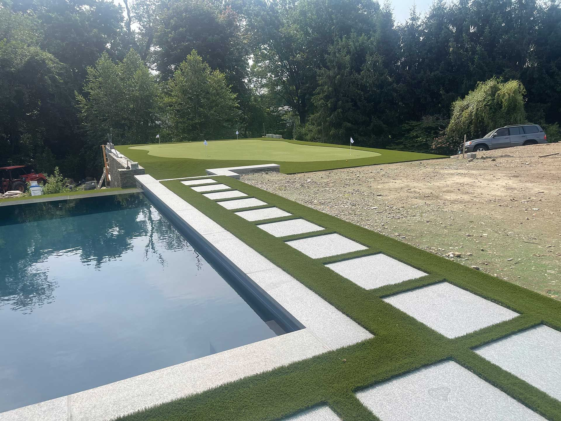 Modern backyard with a swimming pool, stepping-stone path, green lawn, and gravel area beside trees