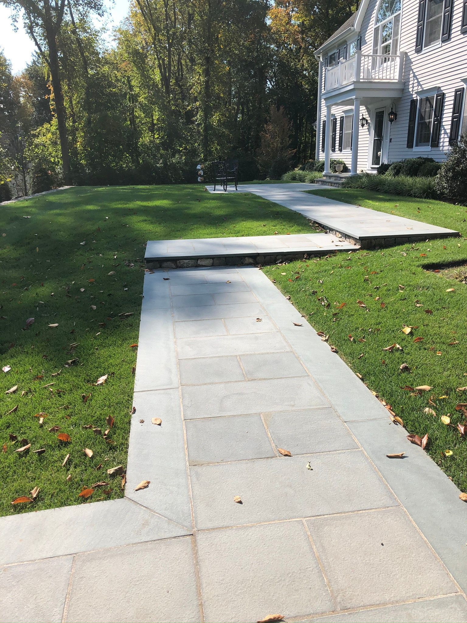 Concrete sidewalk with a raised curb crossing a green lawn beside a white house