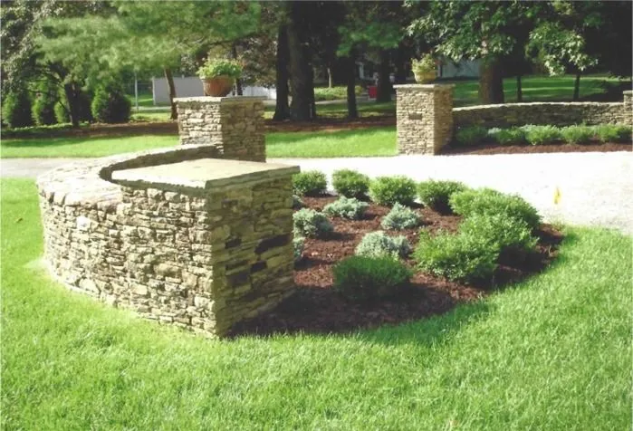 Stone planter and low stone walls surrounding a landscaped flower bed in a green park.