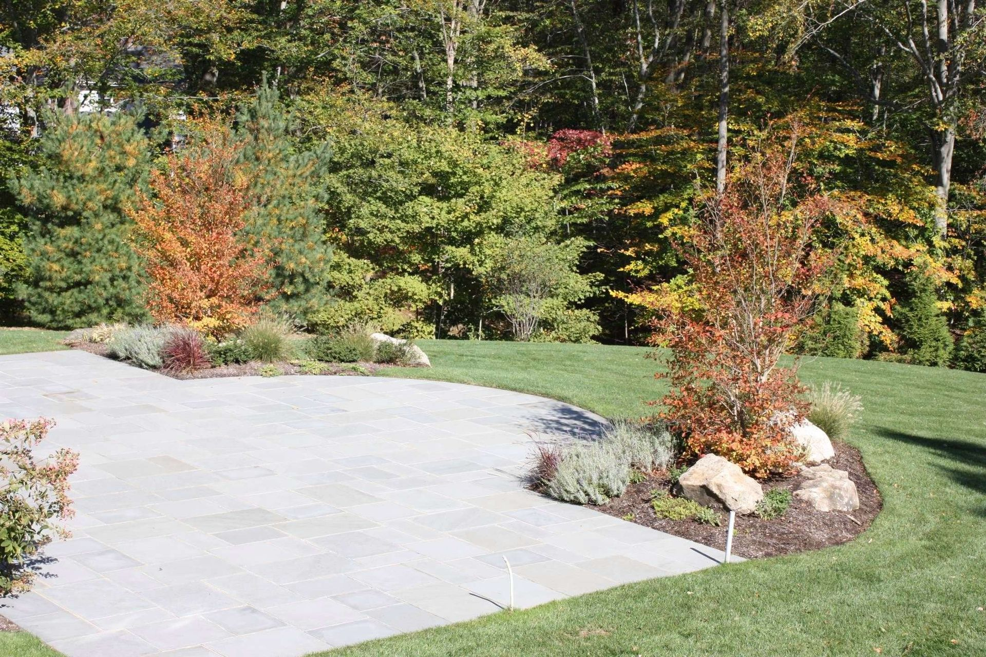 Landscaped garden with stone path, green lawn, and autumn-colored shrubs and trees