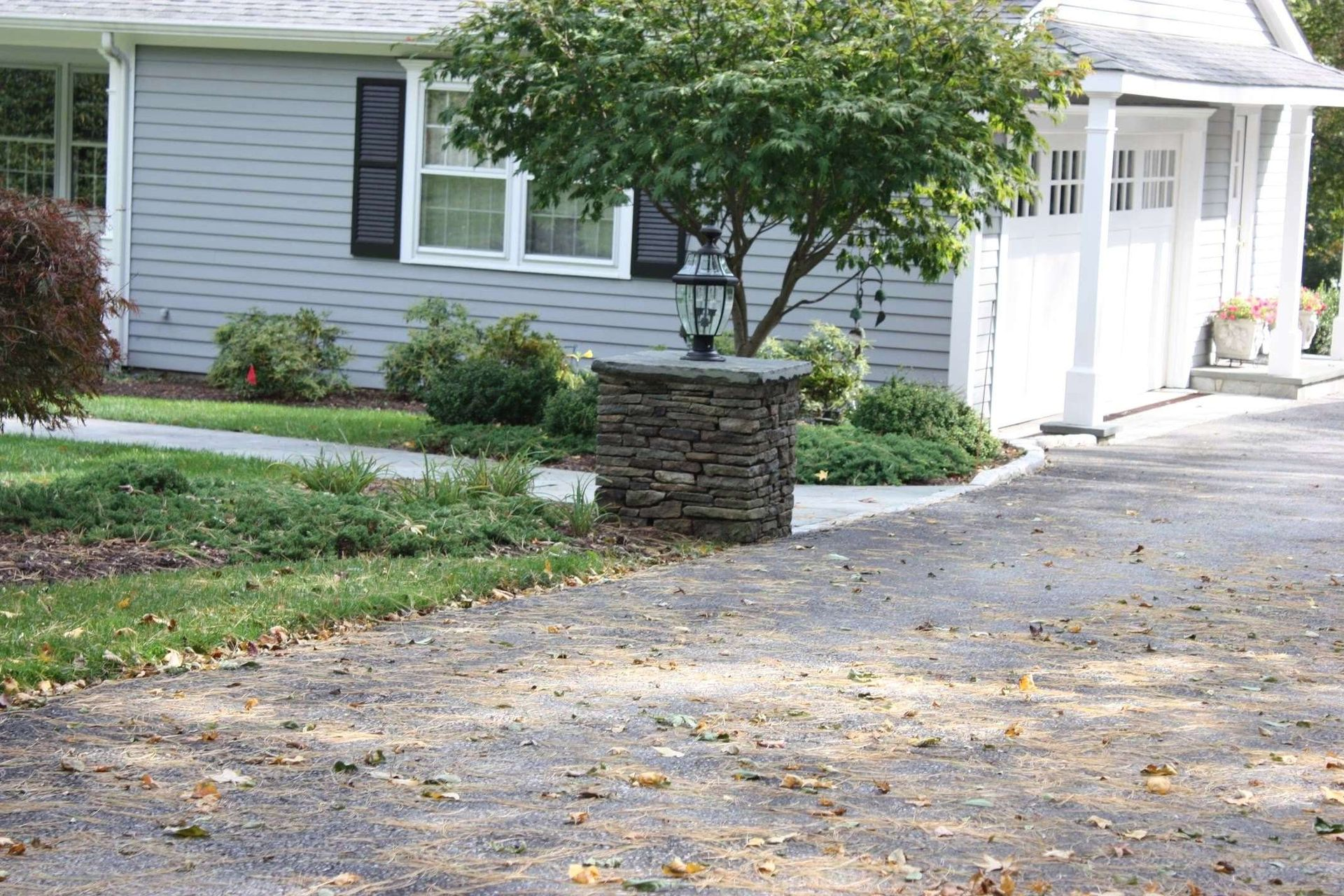 Suburban house with light blue siding, stone mailbox, and a driveway lined with trees and shrubs