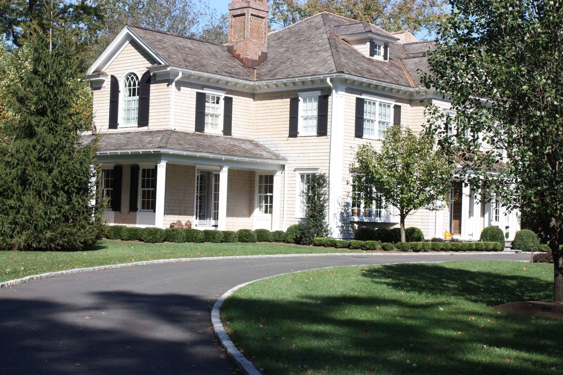 Large white two-story house with a porch, dark shutters, and a curved driveway in the foreground