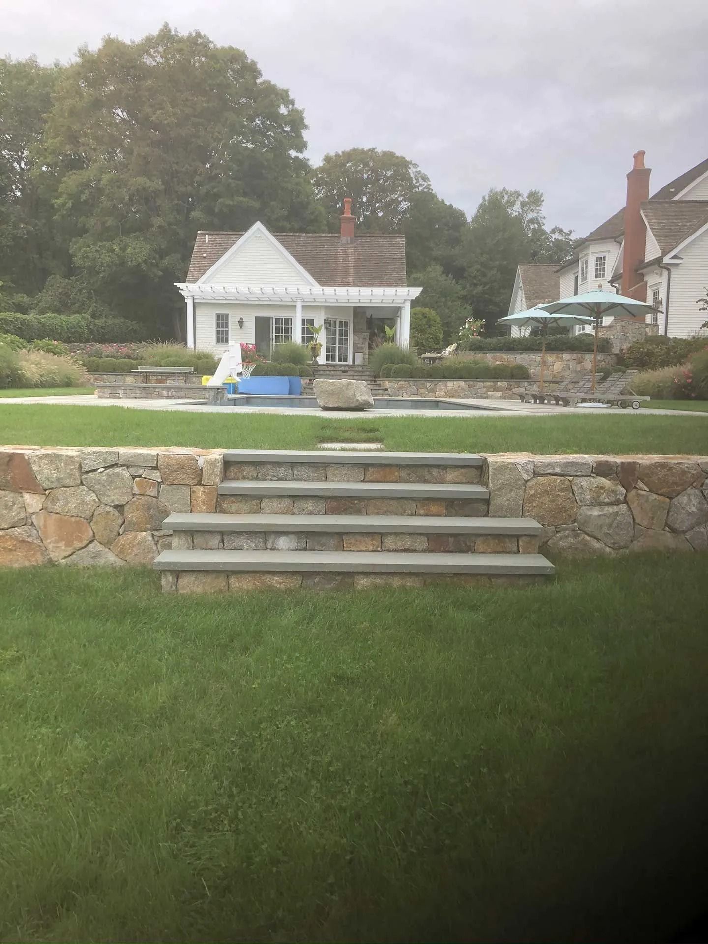 Stone steps lead to a lawn and a white gazebo in a landscaped backyard with neighboring houses.