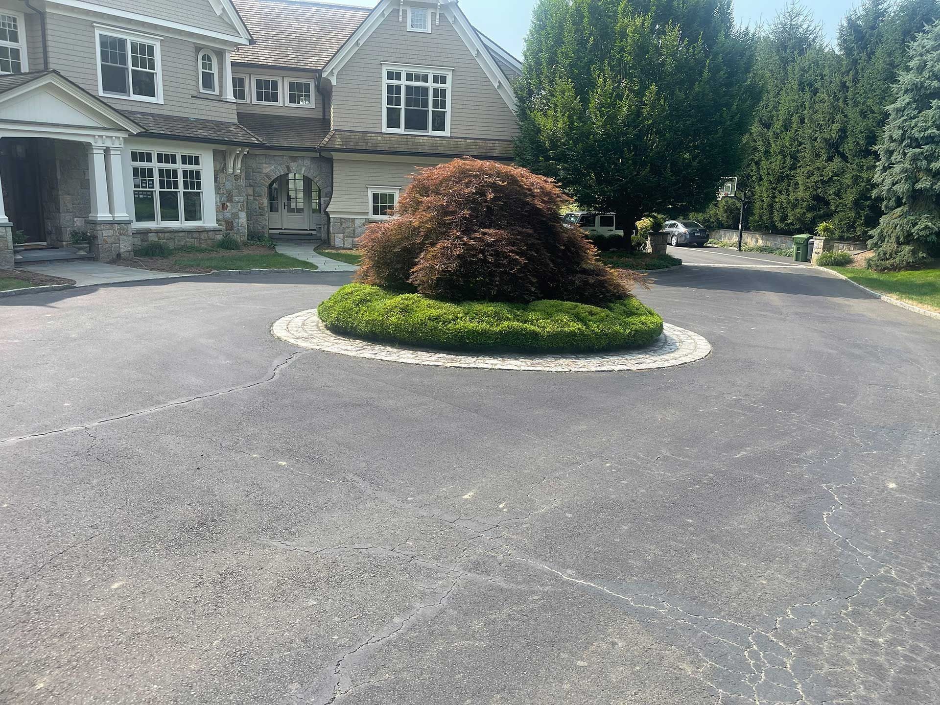 Stone house with large paved driveway and a circular landscaped island of shrubs and flowers