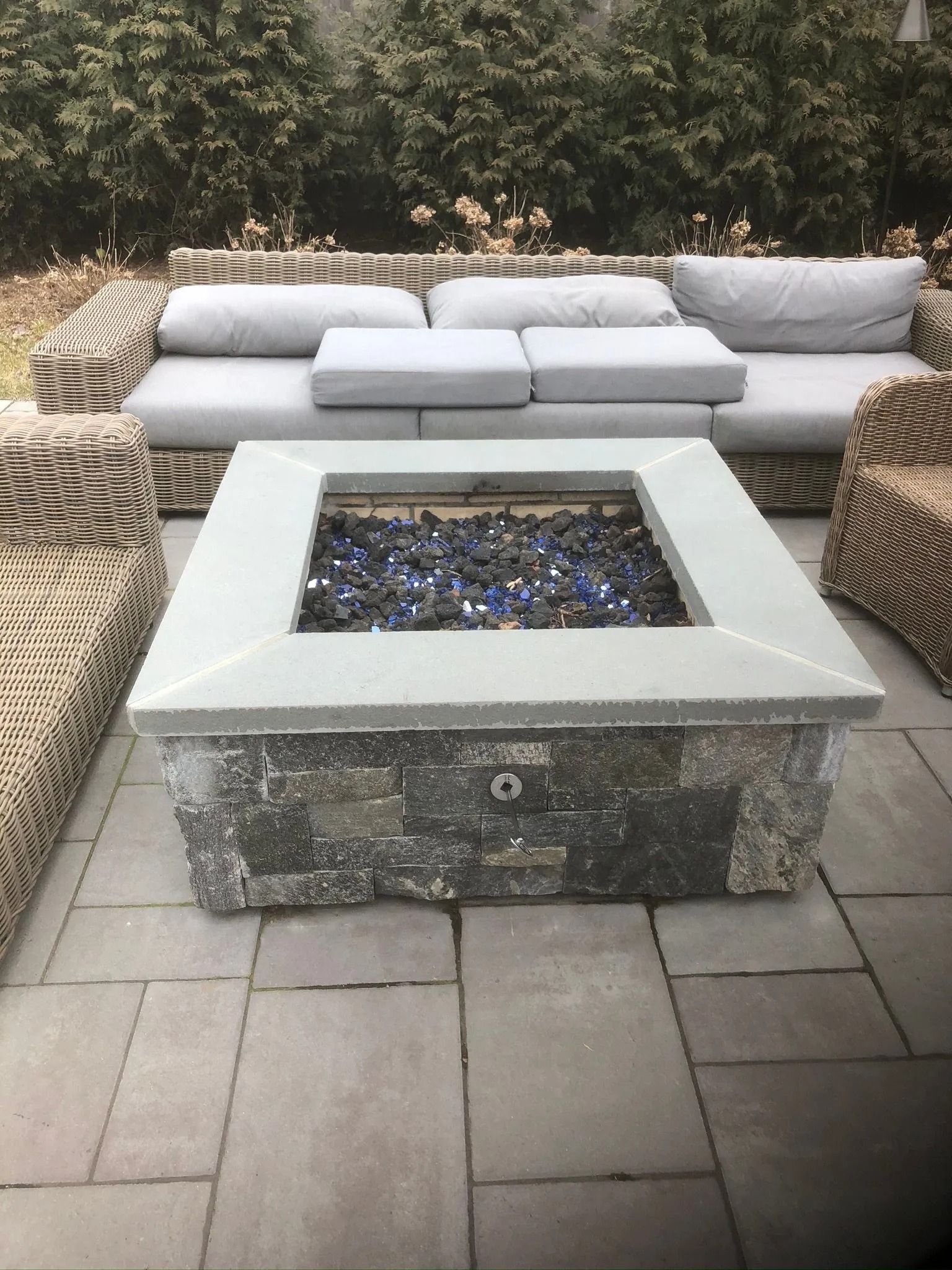 Outdoor patio with cushioned seating around a square fire pit on stone pavers.