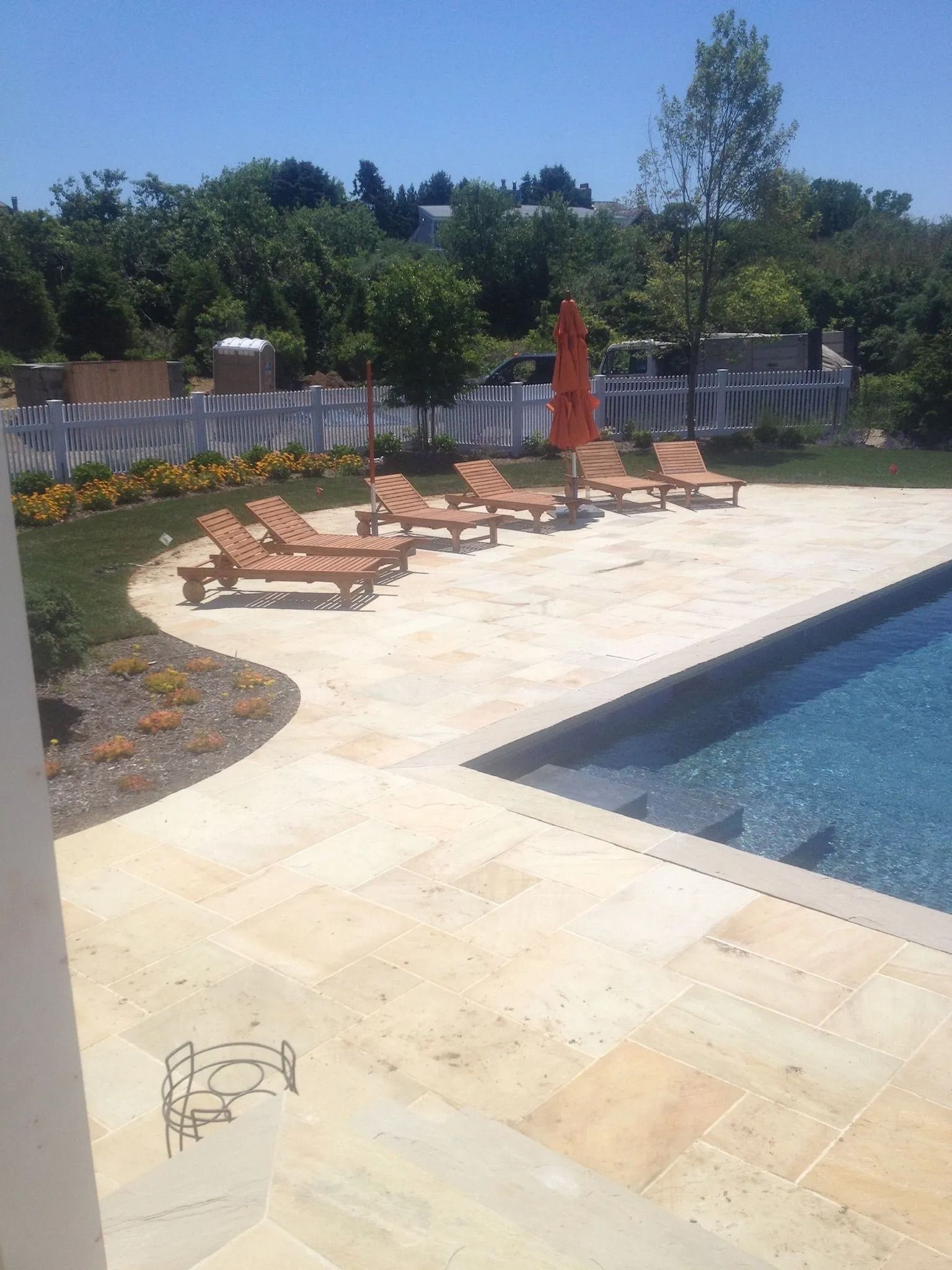 Poolside patio with lounge chairs, red umbrella, and blue swimming pool under bright sun