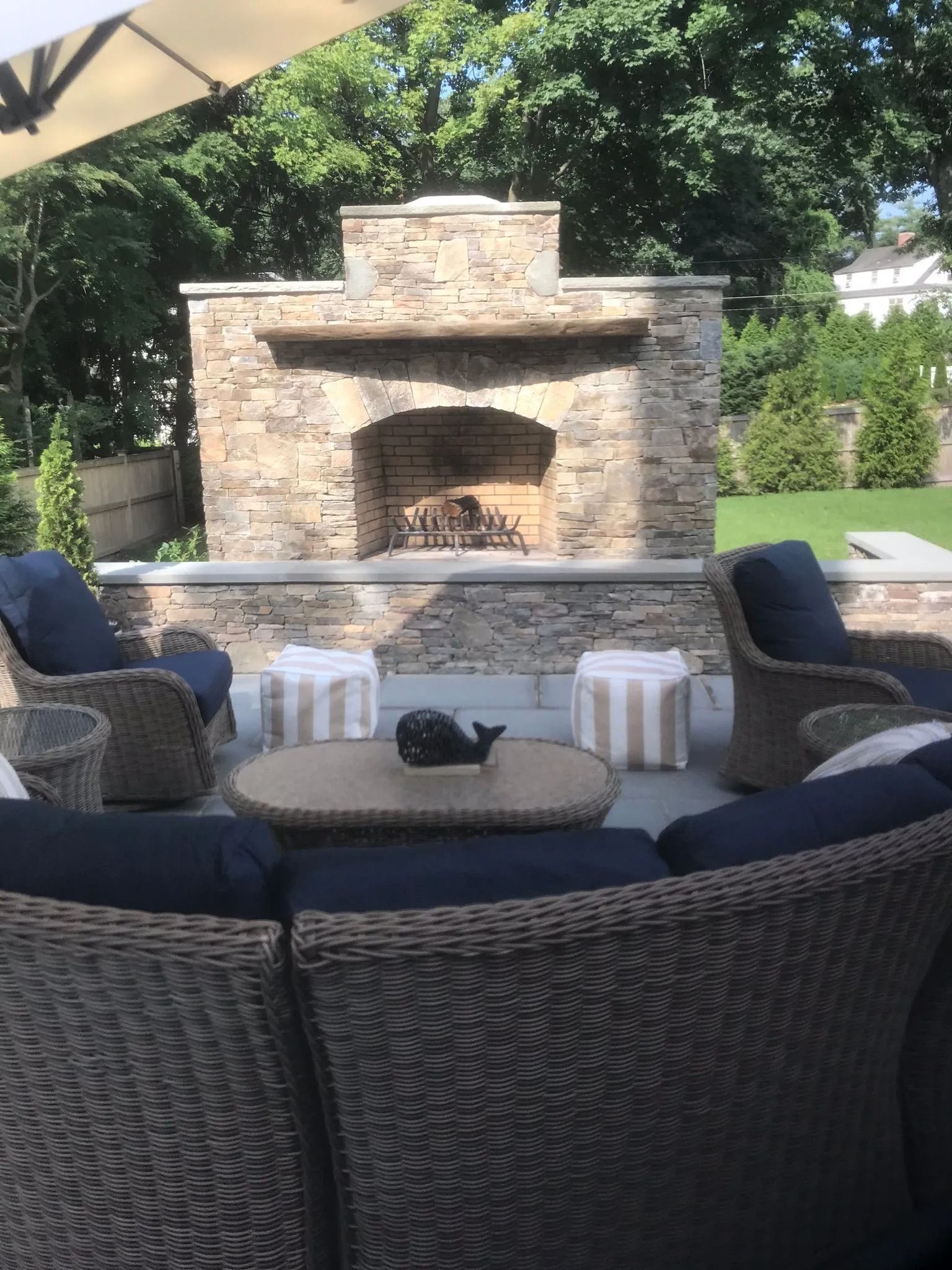 Outdoor patio seating around a stone fireplace in a landscaped backyard