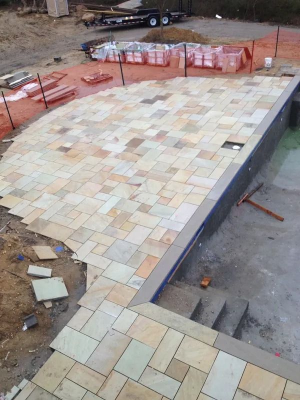 Partially paved patio with multicolored stone tiles and unfinished construction materials nearby
