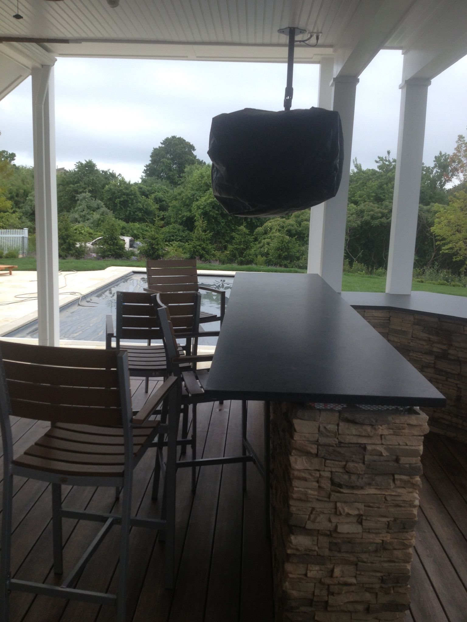 Outdoor patio with black table, wooden chairs, stone bar, and a TV under a covered roof.