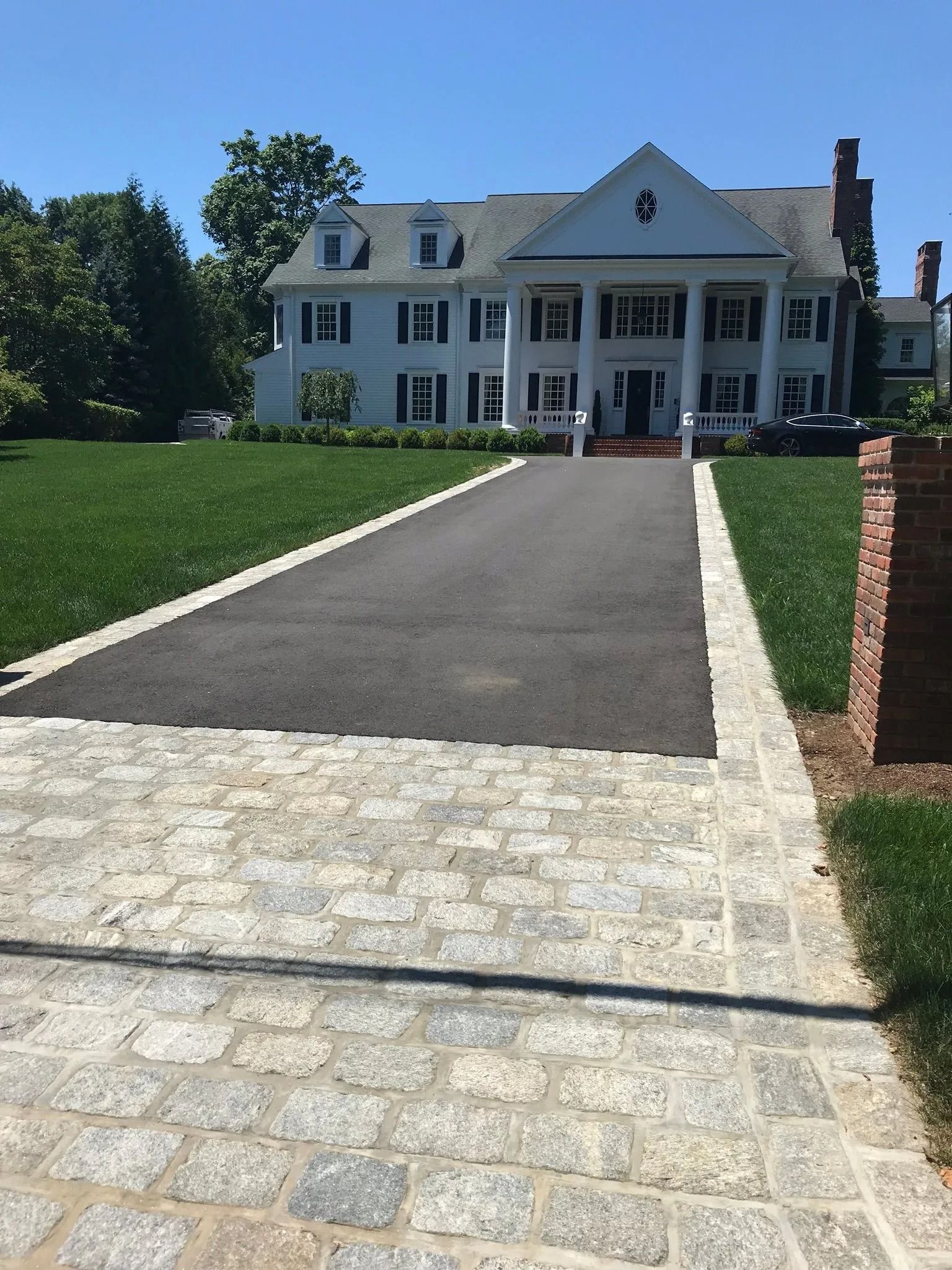 Large white house with a dark driveway and stone walkway leading to the front entrance
