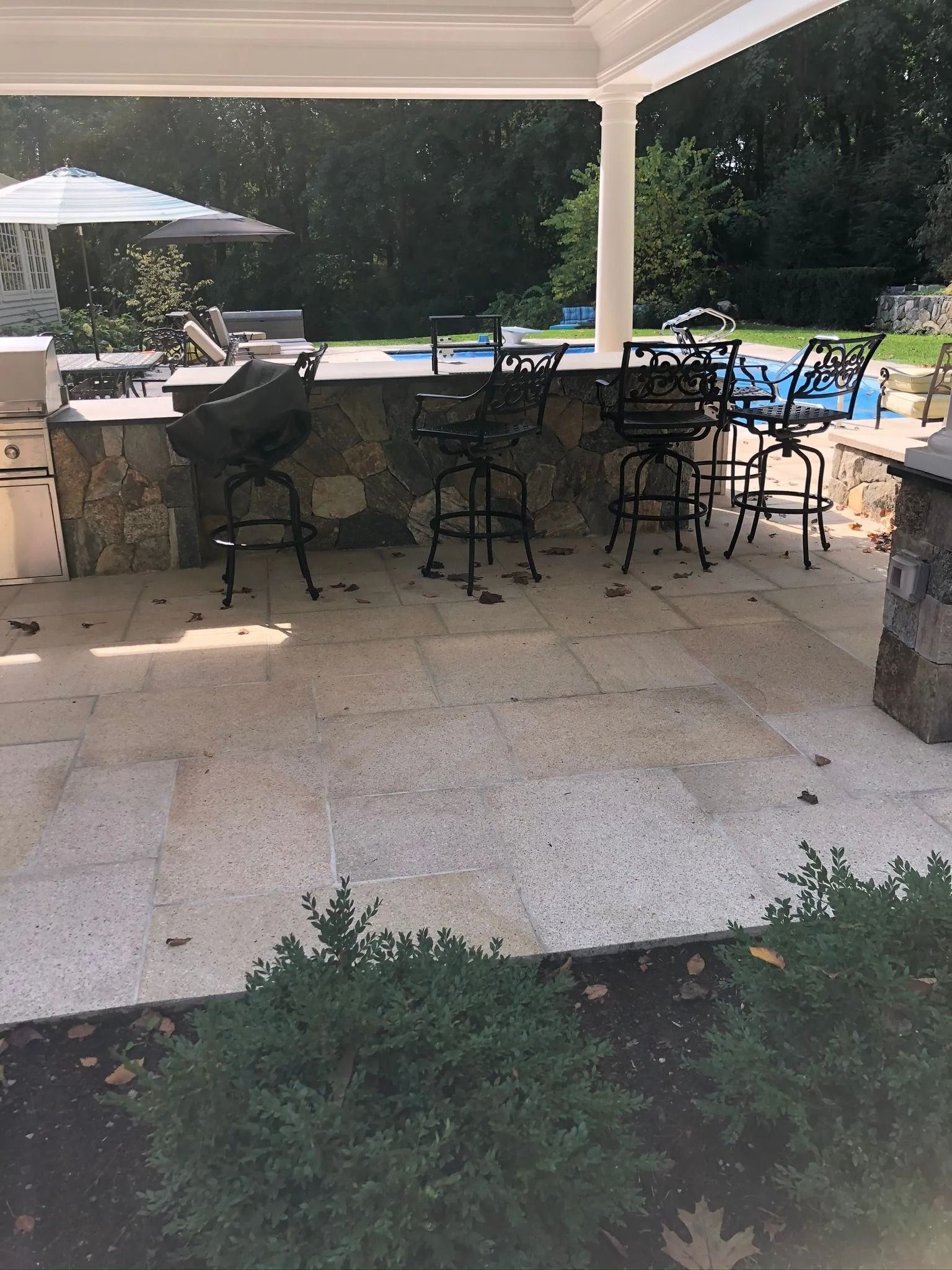 Covered patio with outdoor dining table, black chairs, grill, and poolside lounge chairs in the background