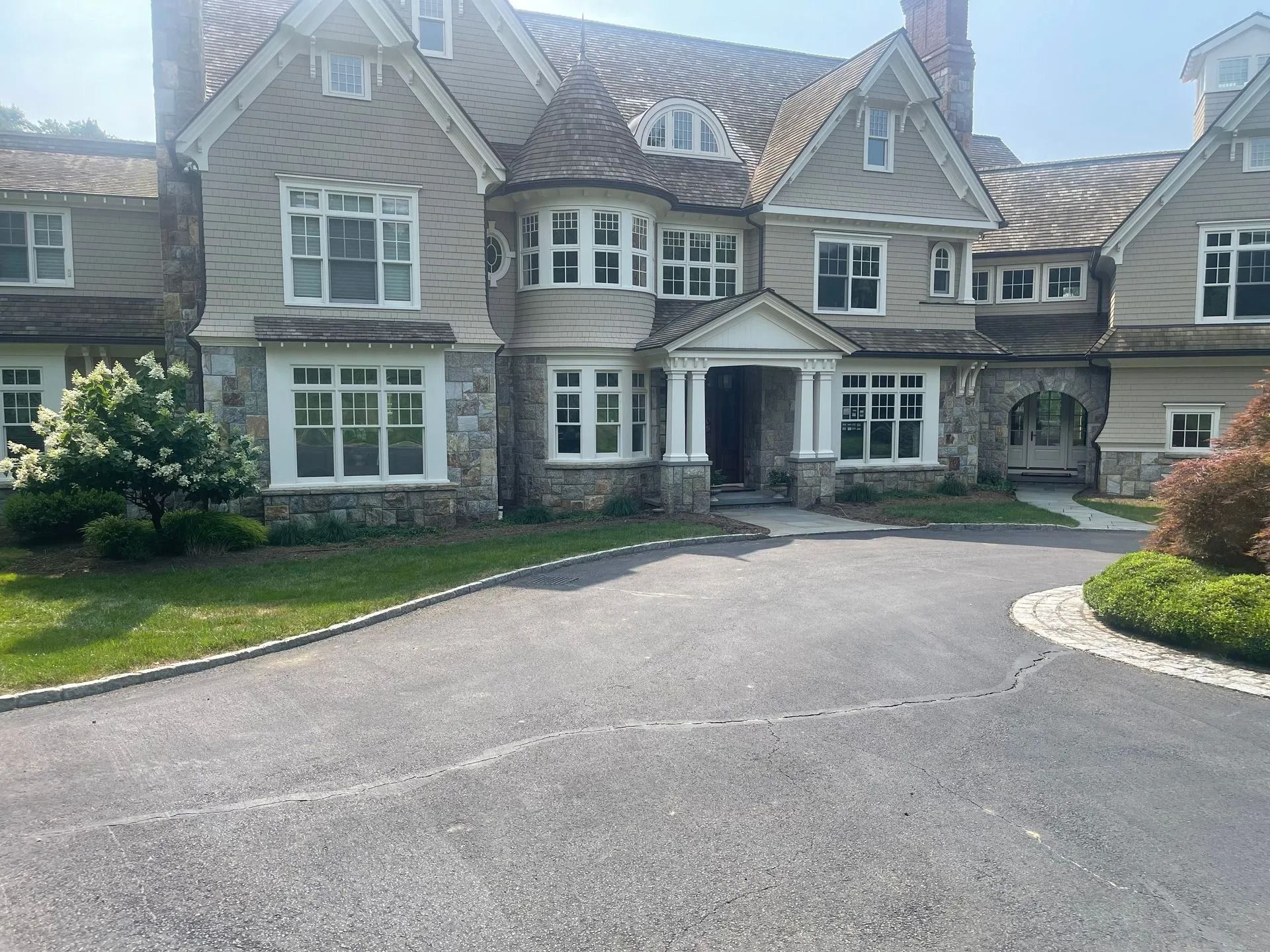 Large stone mansion with arched entry, white-trimmed windows, and a curved driveway in front.