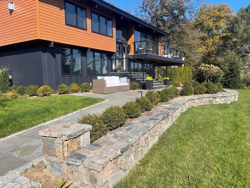 Modern house with orange and black exterior, stone retaining wall, and landscaped lawn in front