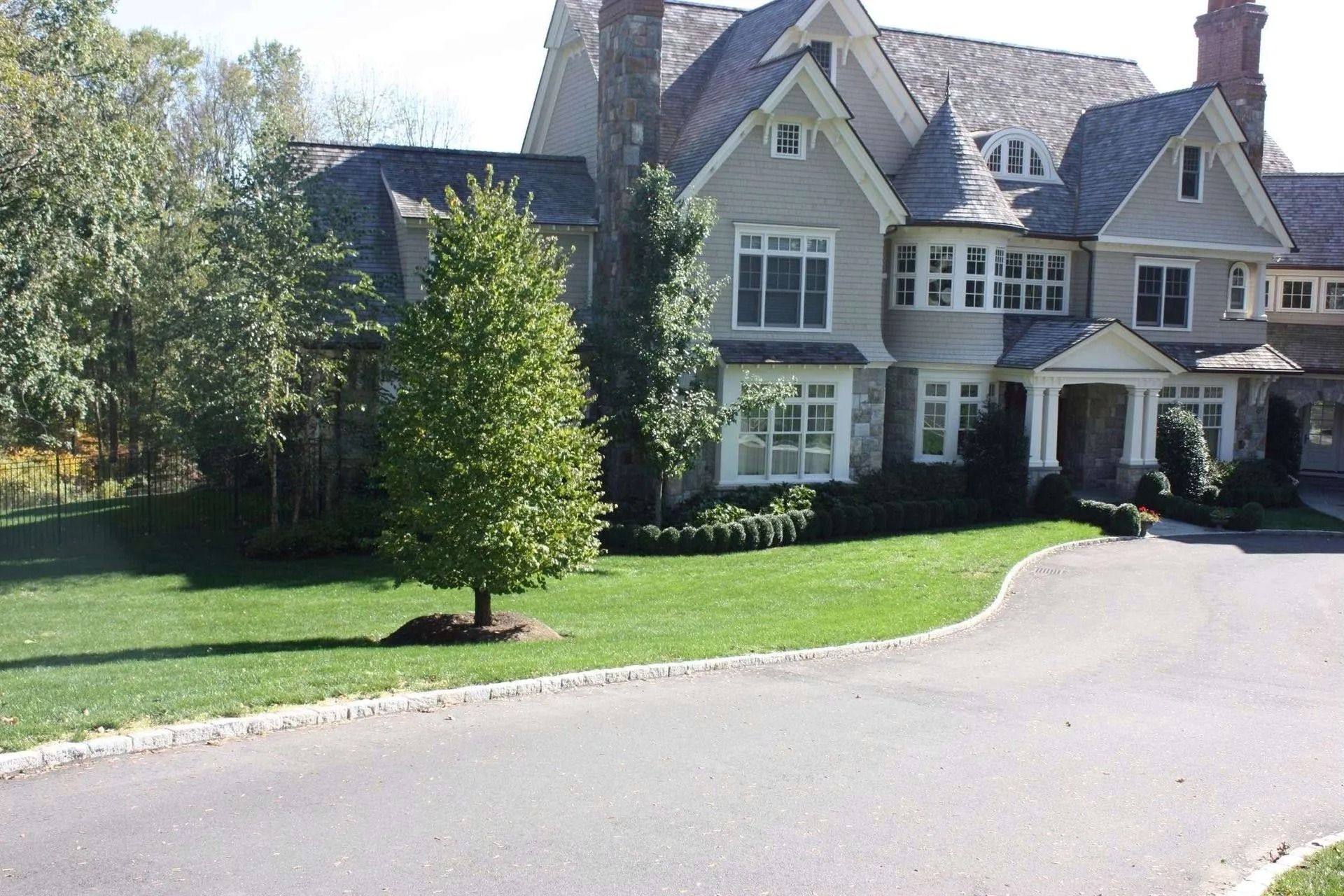 Large gray house with white trim beside a curved driveway and green lawn