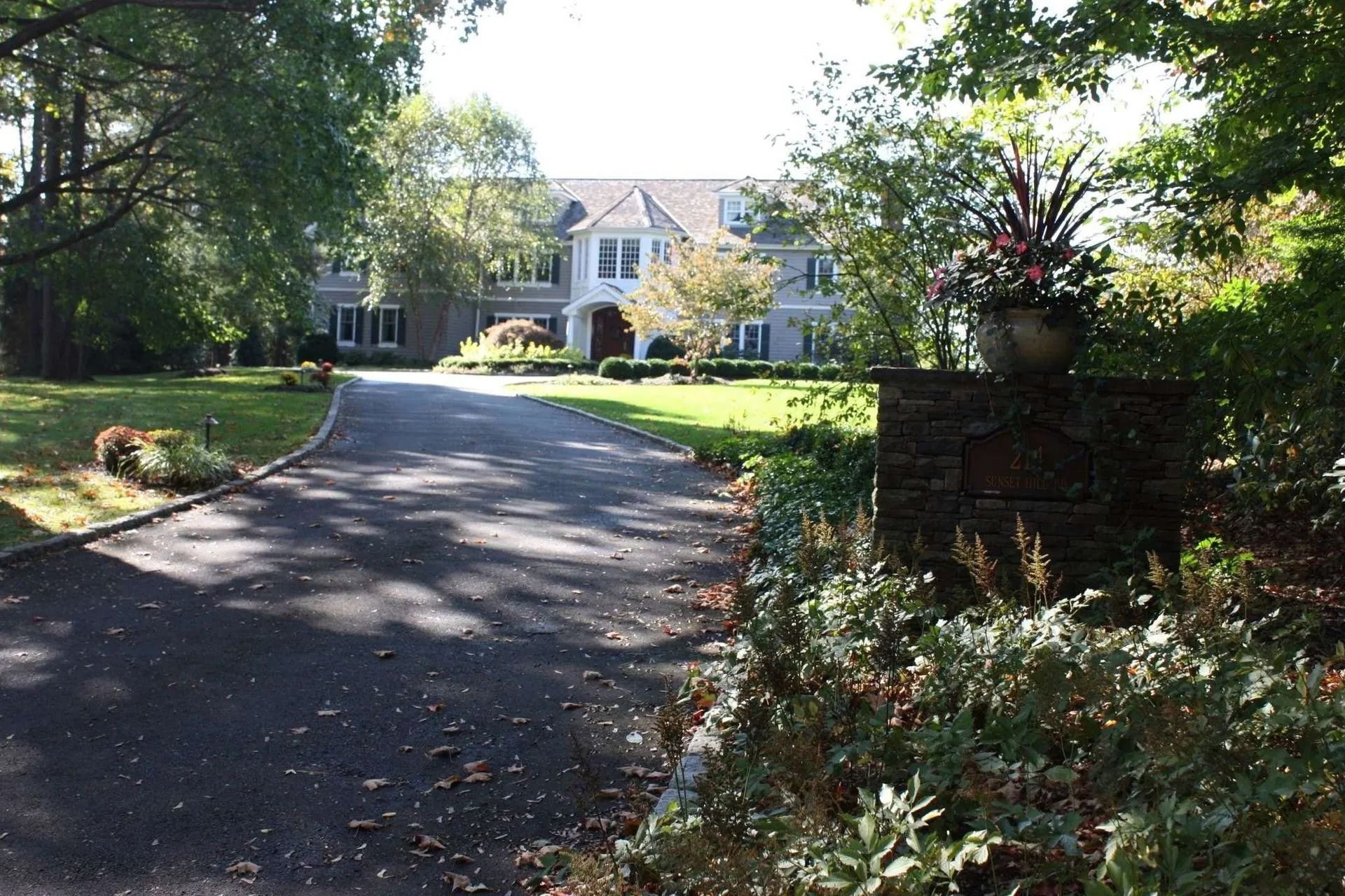 Driveway leading to a large white house with trees and garden landscaping on both sides
