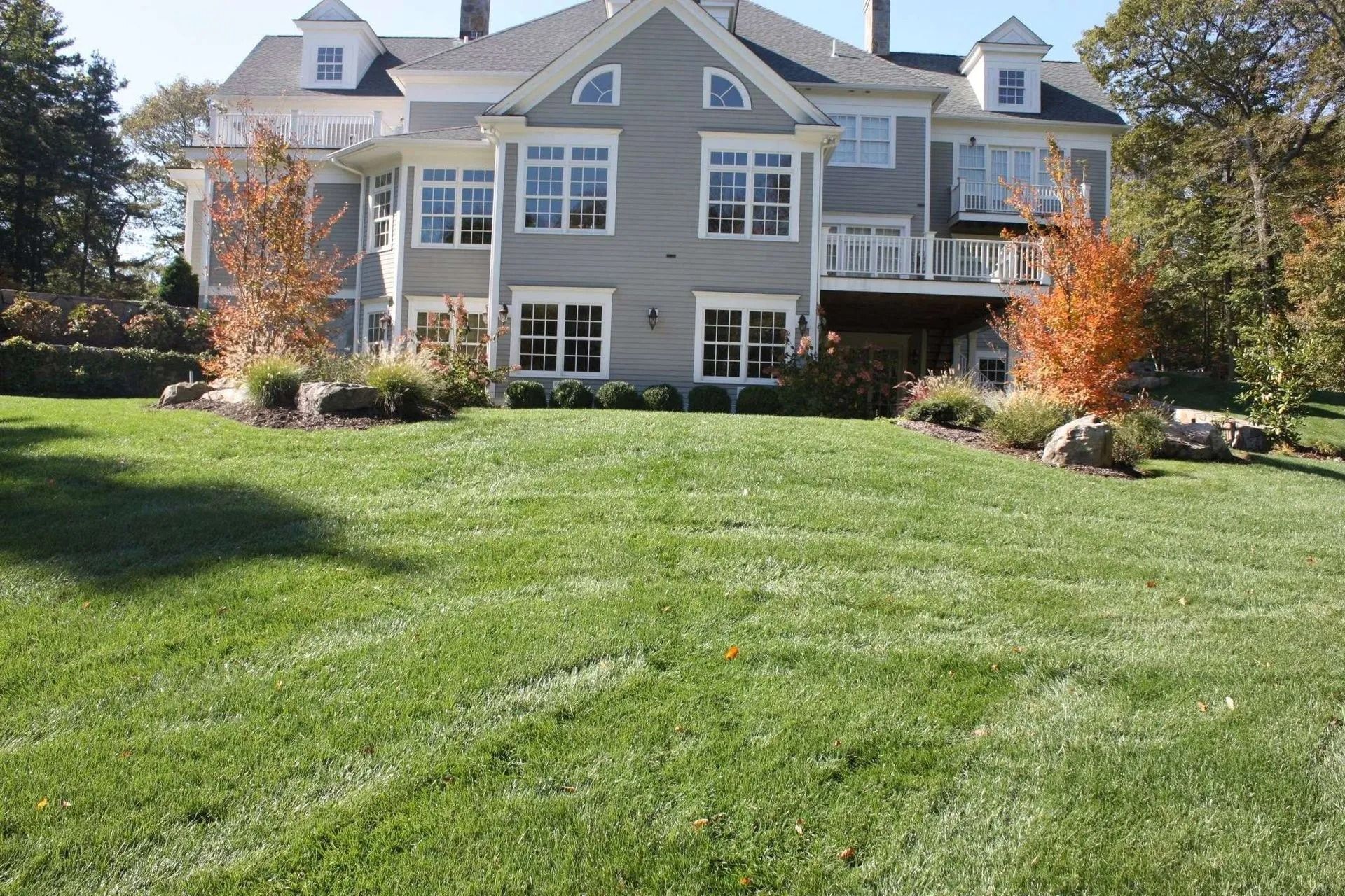 Large gray house with white trim overlooking a green lawn and autumn trees