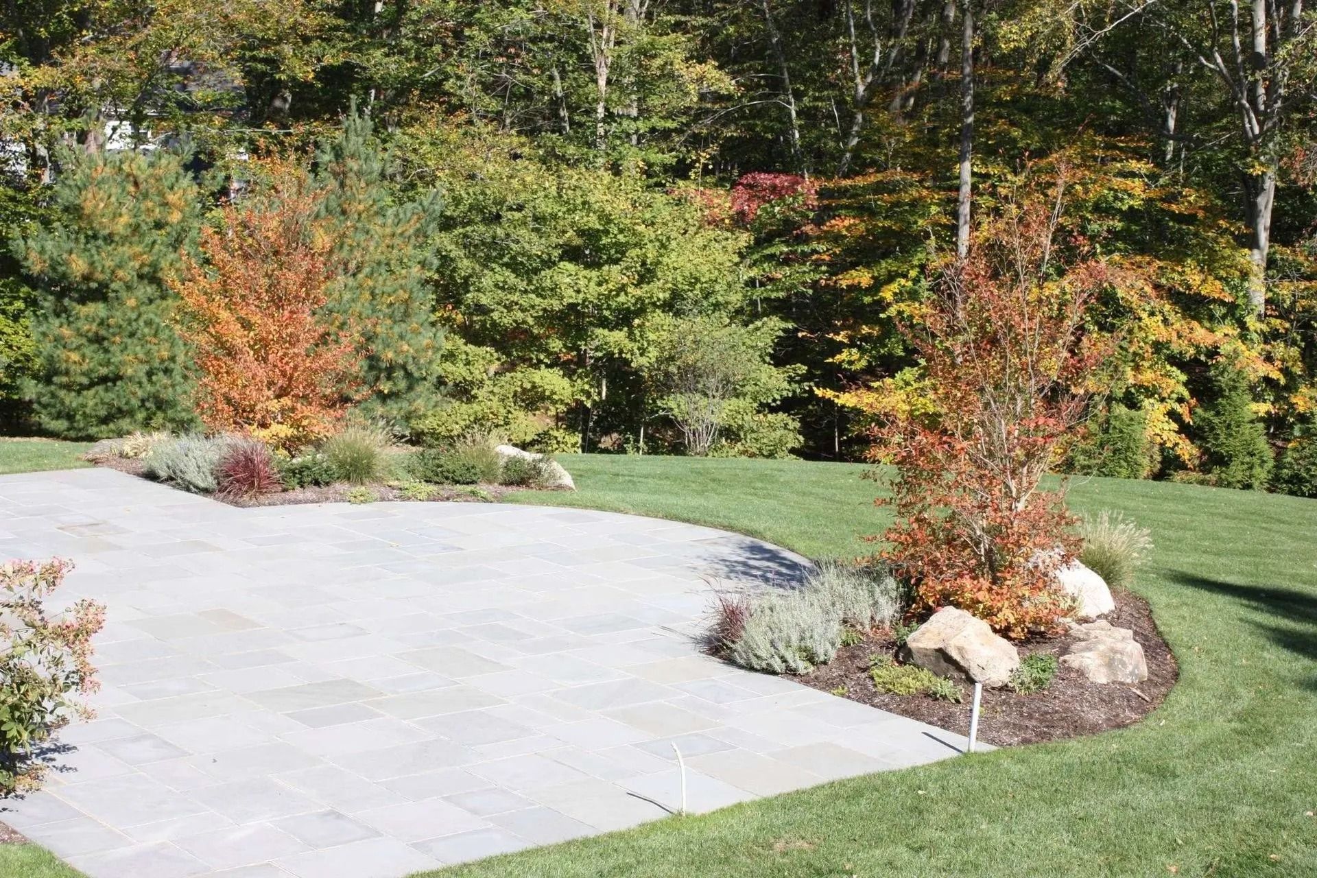 Landscaped garden with a concrete patio, green lawn, and colorful shrubs and trees.