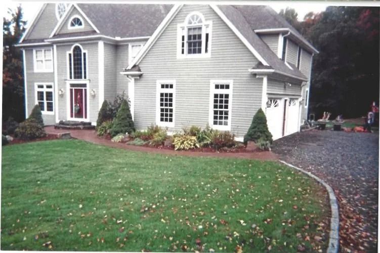 Suburban house with gray siding, white trim, red front door, lawn, and curved driveway