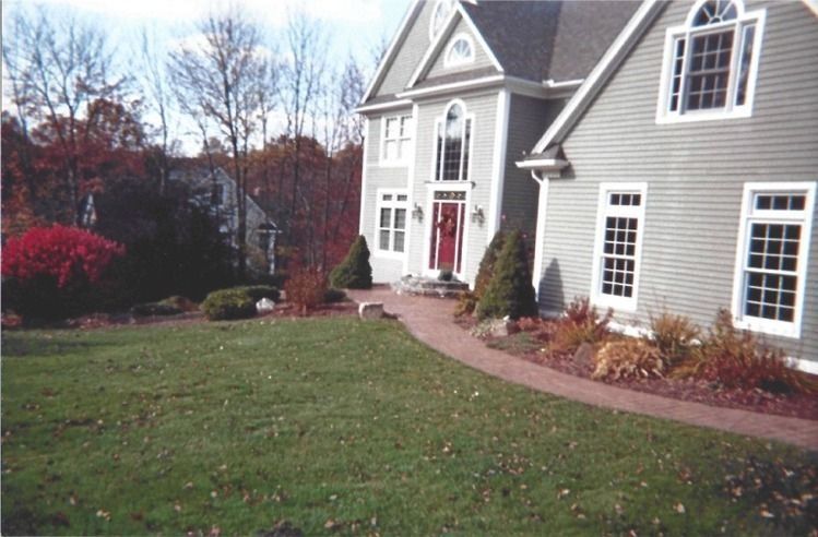 Suburban house with gray siding, white trim, red door, and a curved walkway through a front lawn.