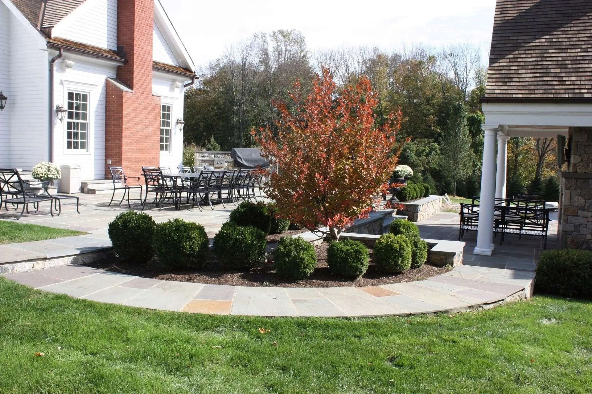 Courtyard with circular garden bed, shrubs, and red-leafed bush beside a brick building and patio chairs