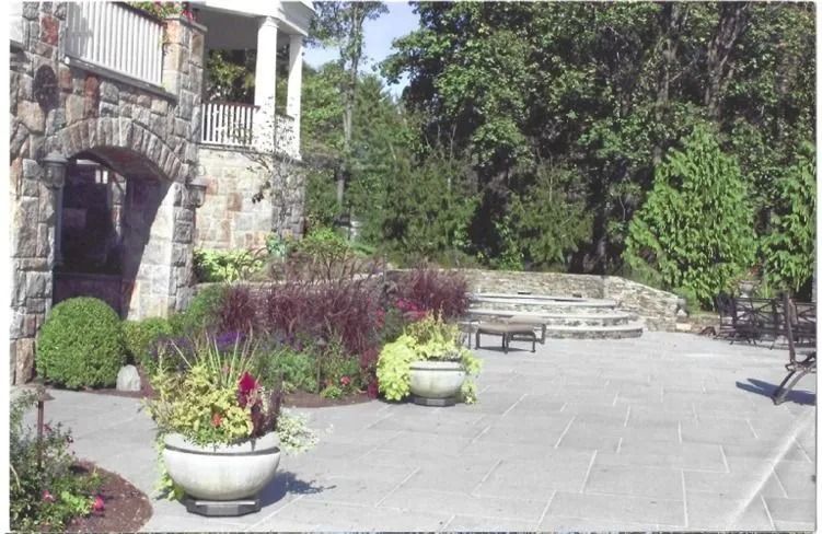 Stone courtyard with potted flowers, benches, and a stone staircase beside greenery