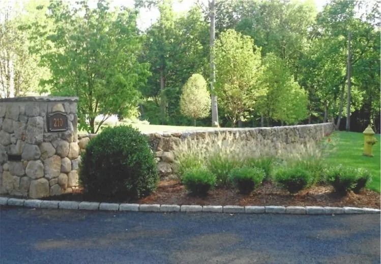 Landscaped stone garden border with shrubs and trees beside a road