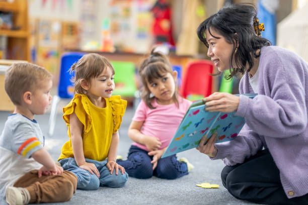 A preschool teacher sits on the floor of her classroom with a small group of students as she reads them a book