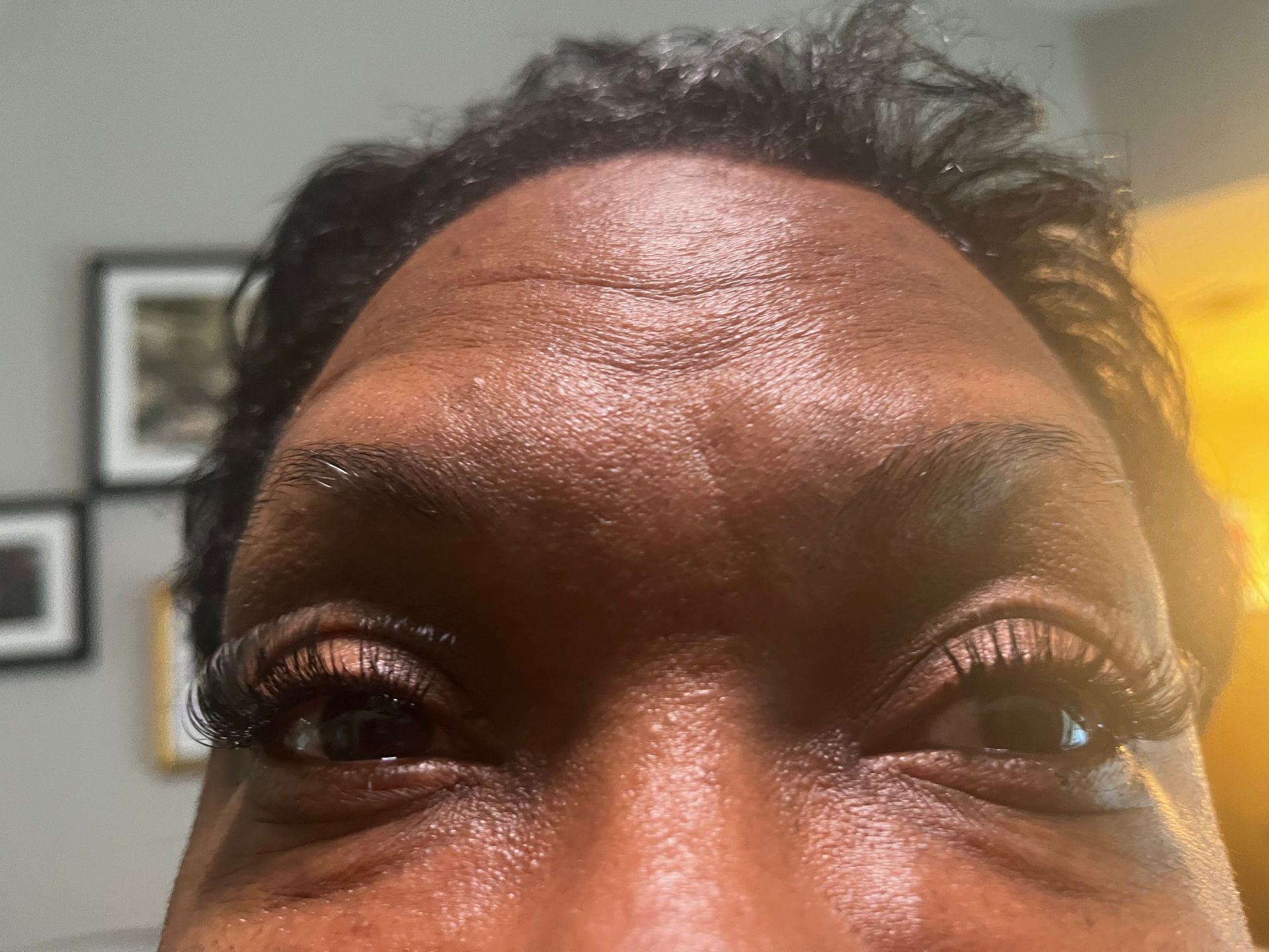 Close-up of a person's eyes and forehead; they have dark skin and long eyelashes. The forehead appears shiny.