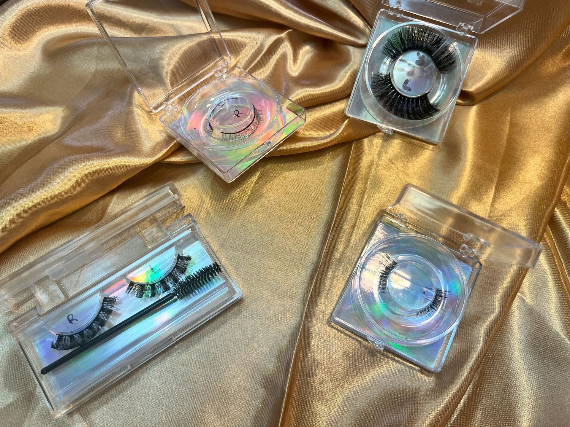 Four pairs of false eyelashes in clear plastic cases on gold fabric.