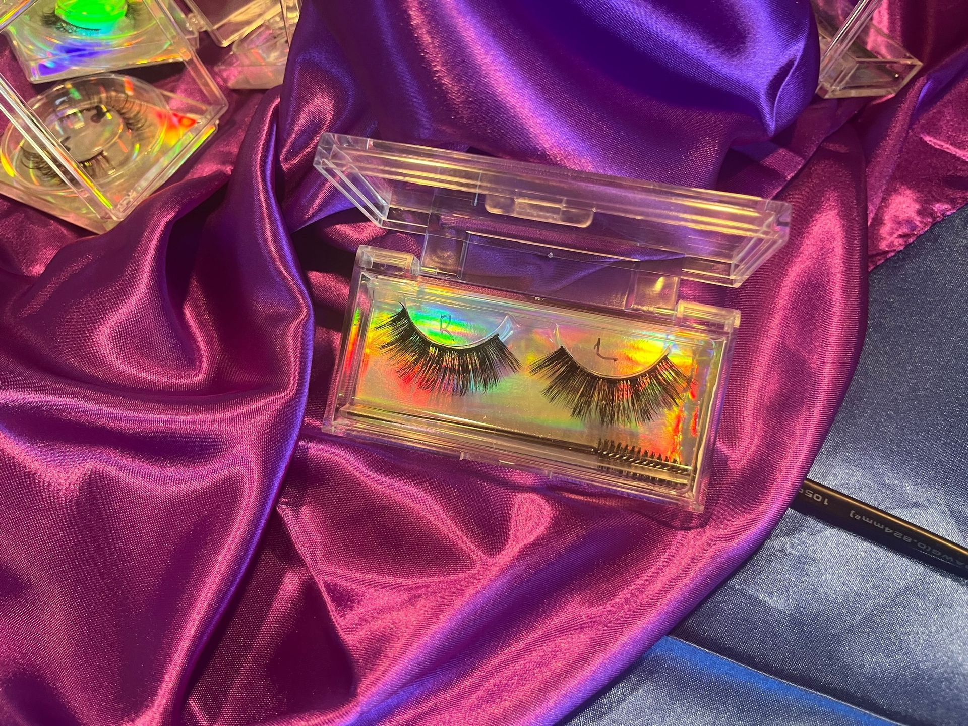 Clear plastic case with false eyelashes on purple satin fabric.