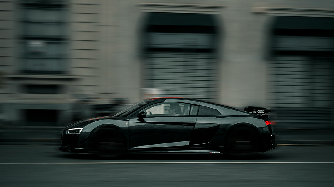 Black sports car speeding down a city street with a blurred background of buildings.