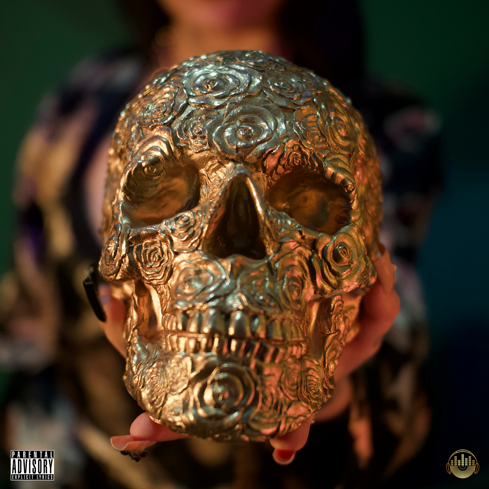 Golden skull with rose patterns, held by unseen hands. Green and dark background, with a 