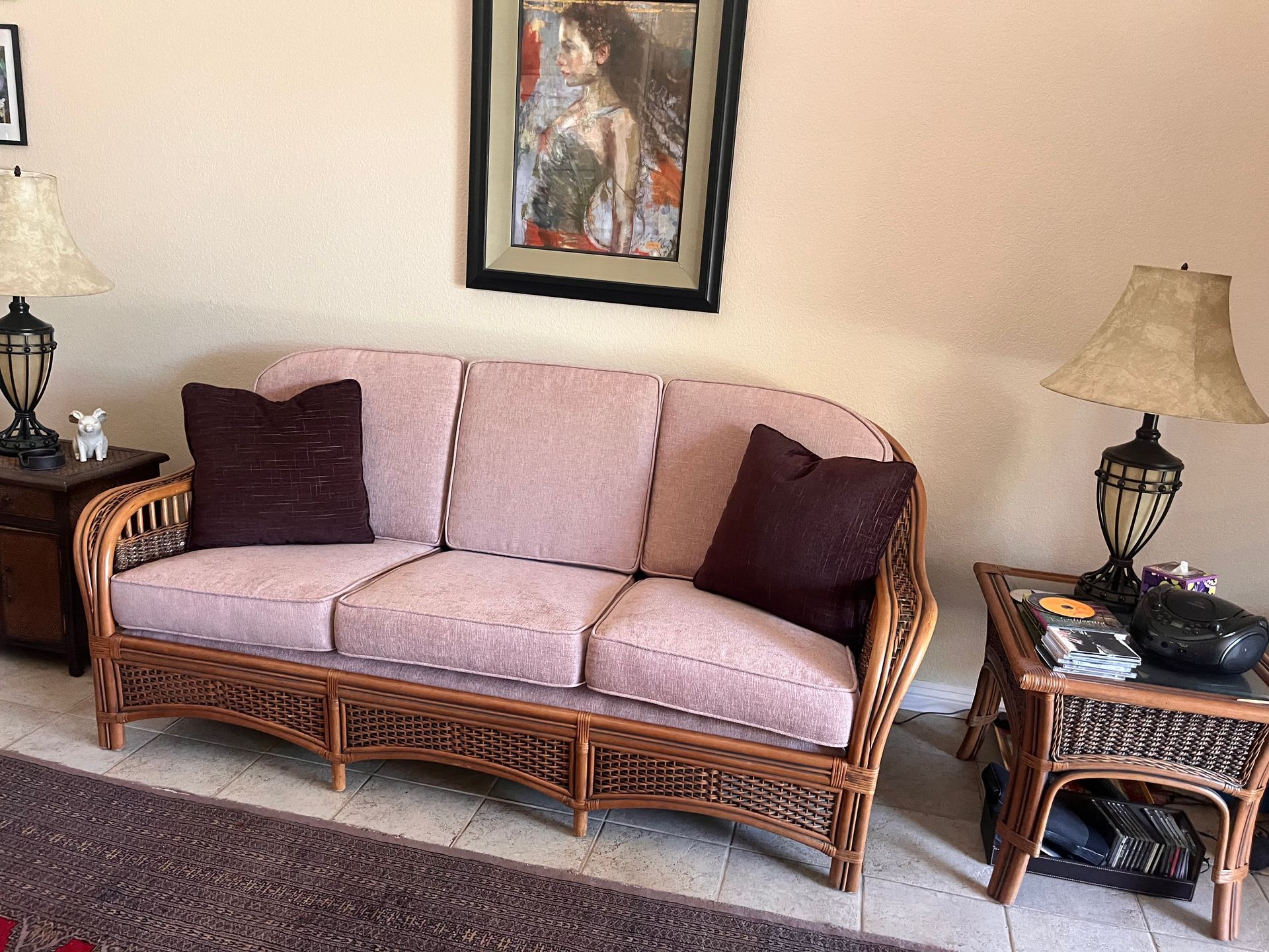 Living room with a wicker sofa, purple cushions, and matching side tables beneath framed wall art