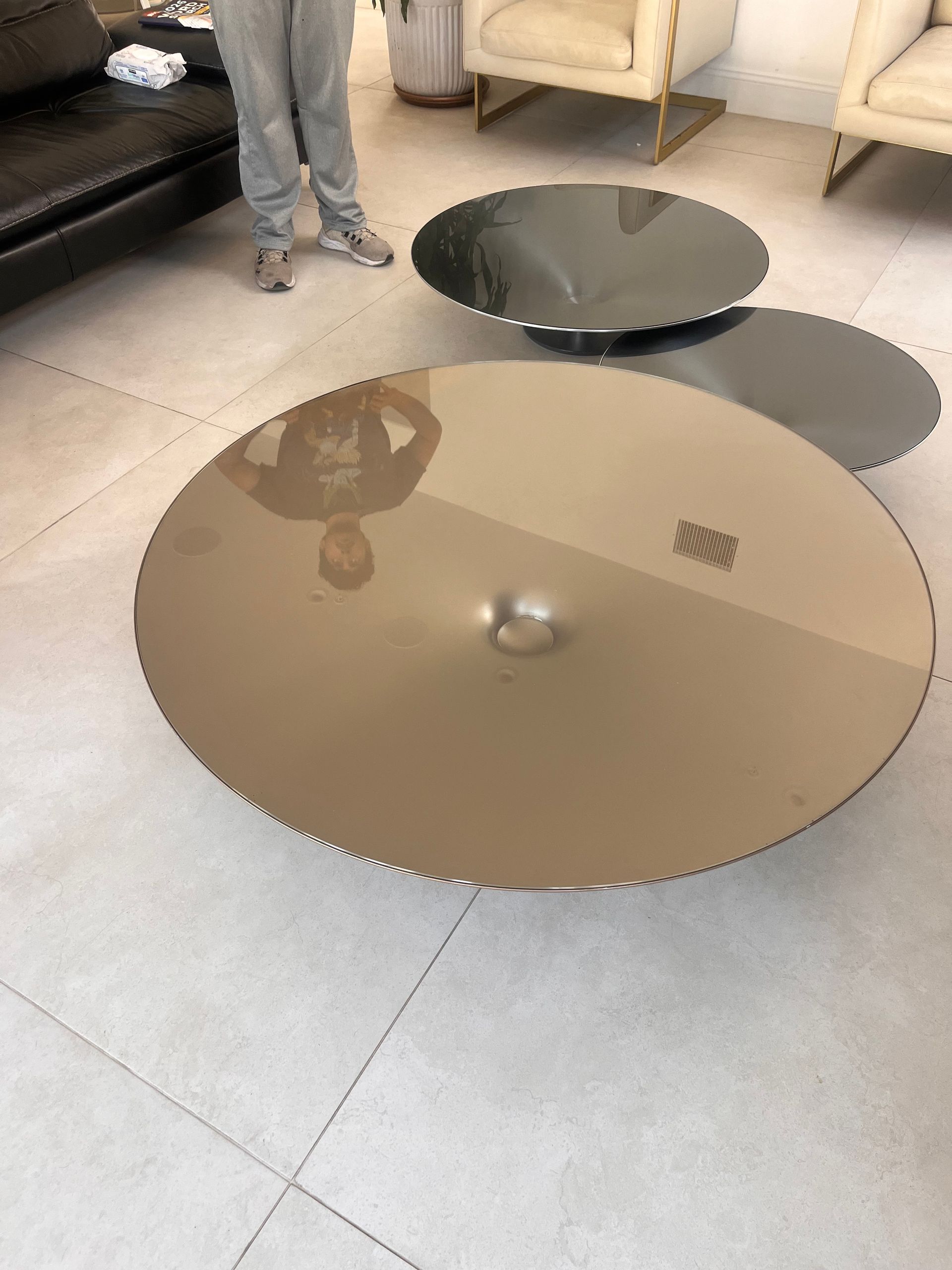 Two glass coffee tables on a tiled floor in a living room, one bronze and one dark gray.