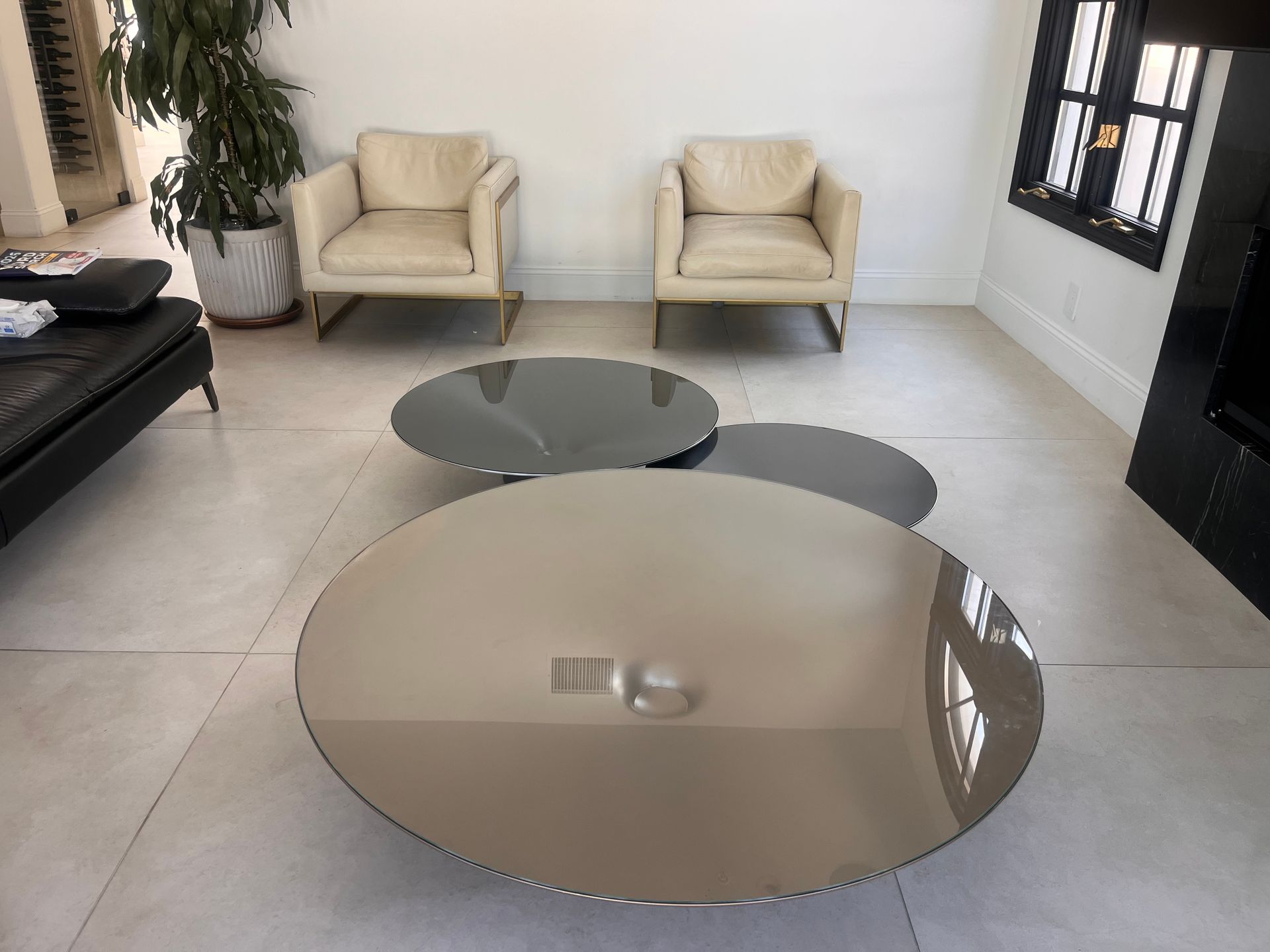 Modern living room with two beige chairs and two round glass coffee tables on a tiled floor