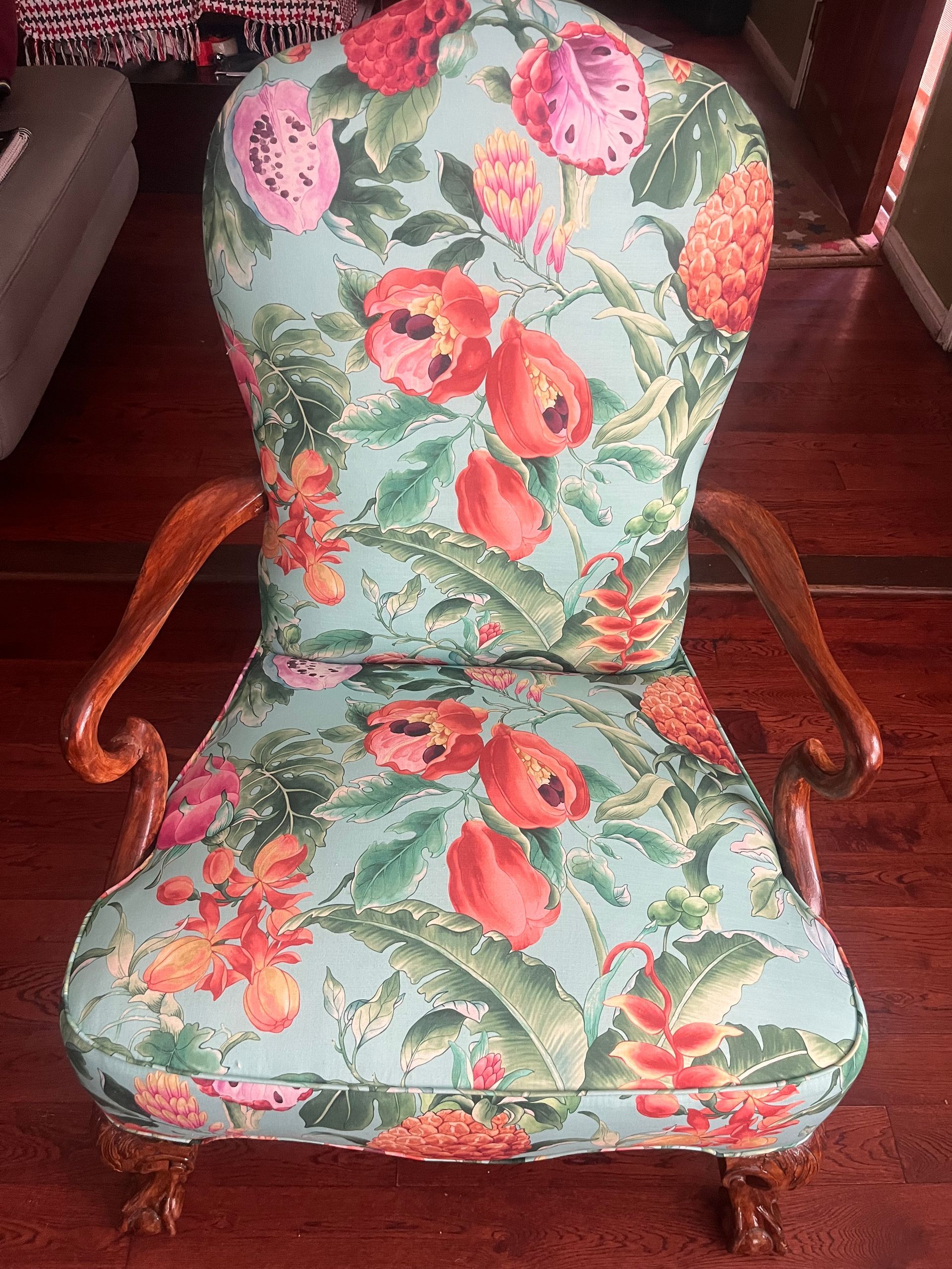 Floral upholstered armchair with curved wooden arms and legs, in green, pink, and red.