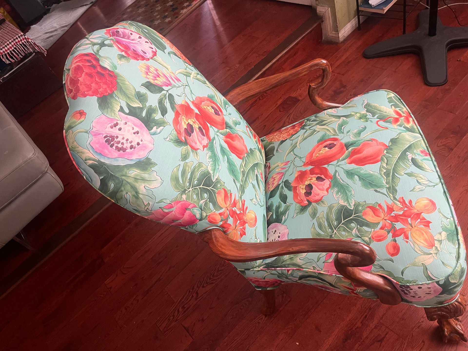 Floral upholstered chair with wooden arms on a hardwood floor in a living room.