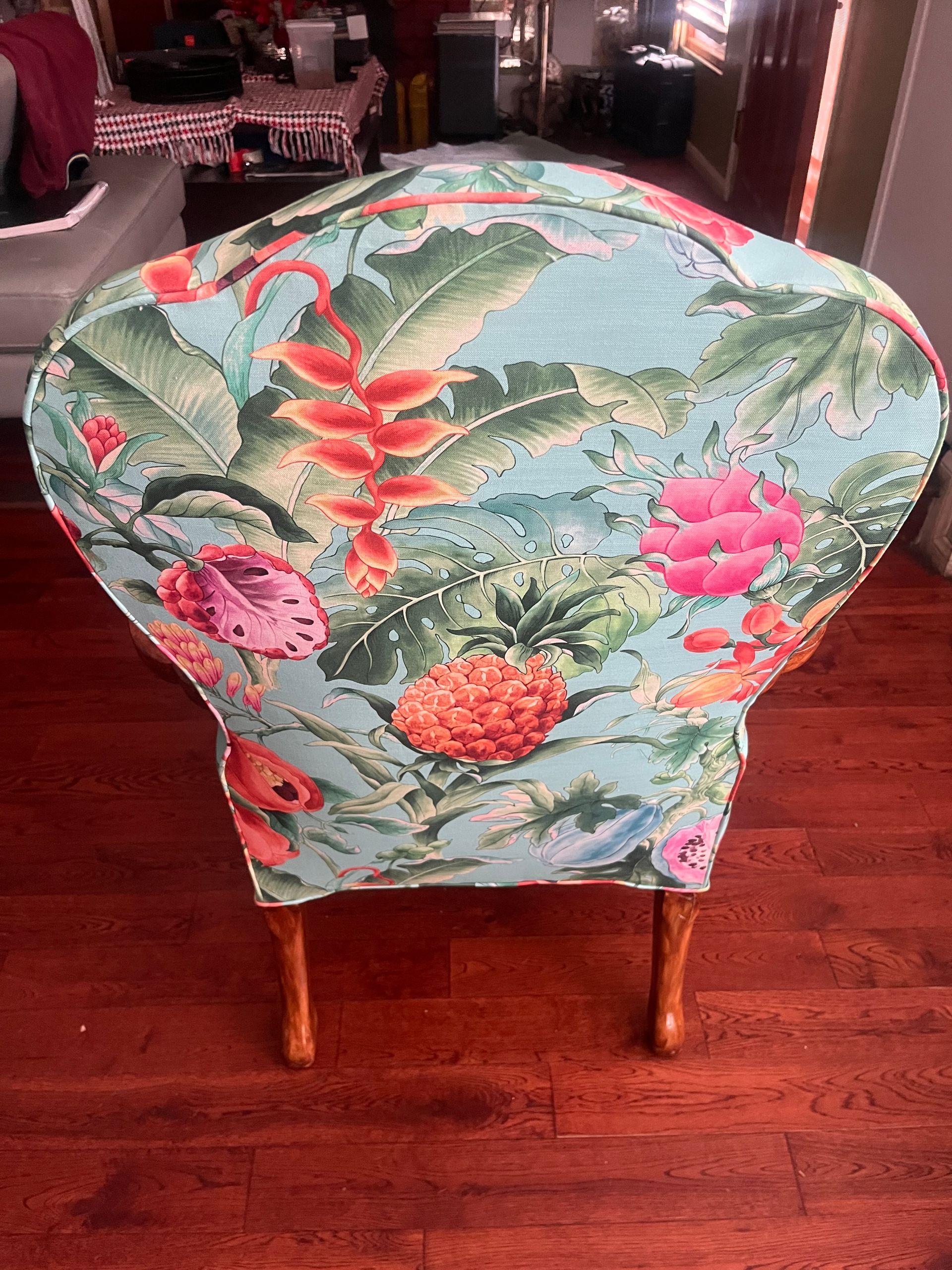 Floral upholstered chair with green, pink, and red tropical print on a hardwood floor